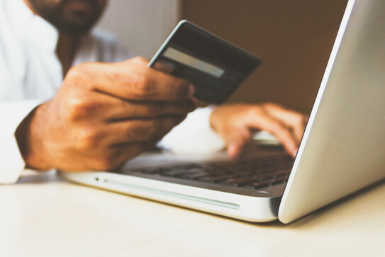 A person holding a credit card while typing on a laptop computer | WooCommerce for Ecommerce